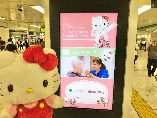 デジタルサイネージの前で満足するキティちゃんの写真